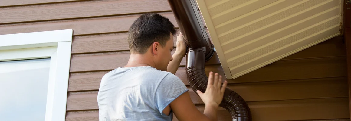 Person montiert Fallrohr an Hauswand.